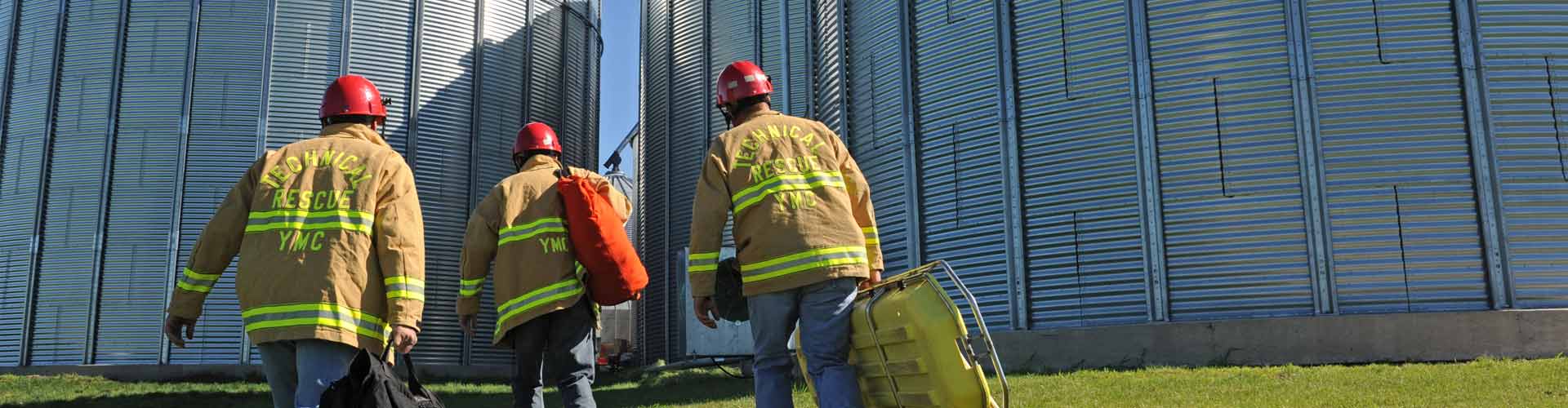 Firefighters walking towards grain bins while holding safety equipment
